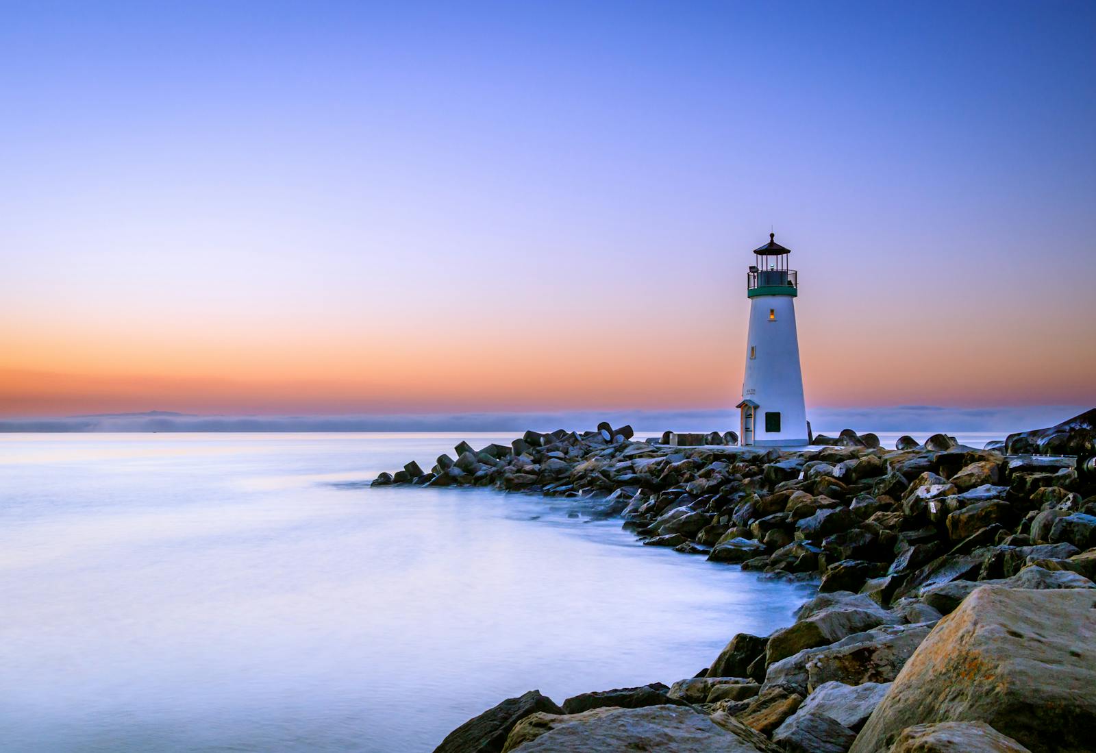 Lighthouse on rocky breakwater at golden hour, dependable through the seasons
